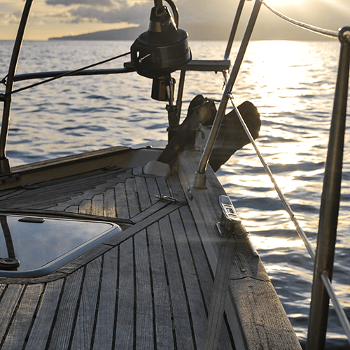 Overlooking the ocean into the sunset over the bow of a well-loved rustic sailboat.