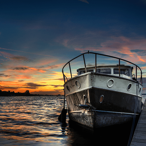 Well-loved boat docked alongside a pier at sunset.